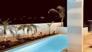 Ein moderner Außenpoolbereich mit einem klaren, blauen Pool, umgeben von Palmen und einem Steinboden.