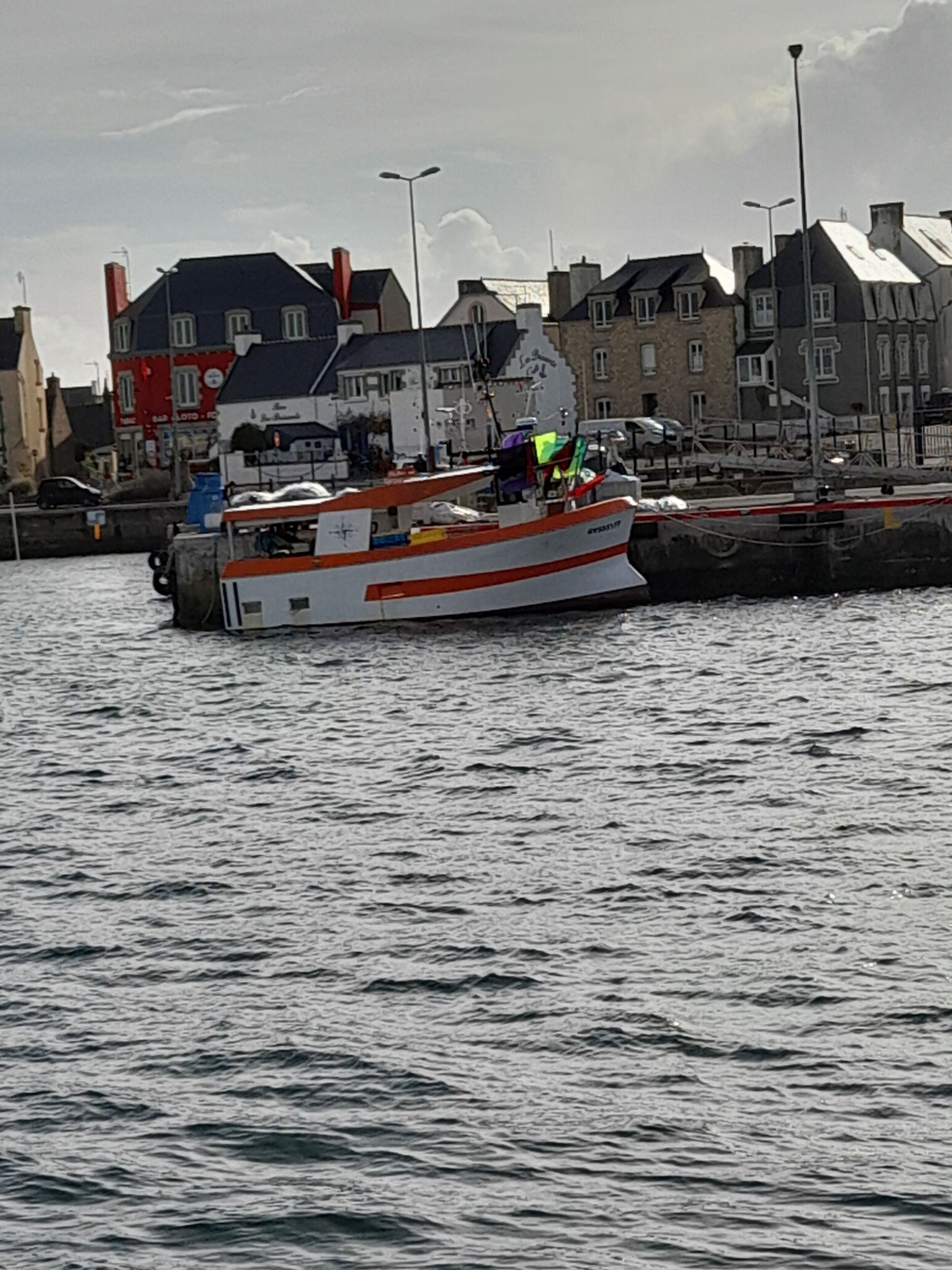 A boat docked at a pier with buildings in the background.