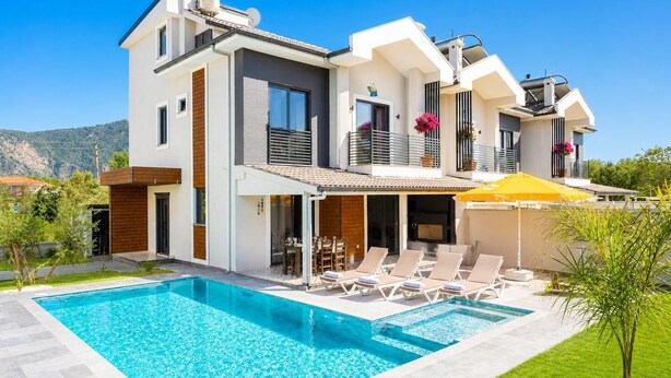 Une maison moderne à deux étages, dotée d’une piscine, d’un espace salon extérieur et offrant une vue sur les montagnes.