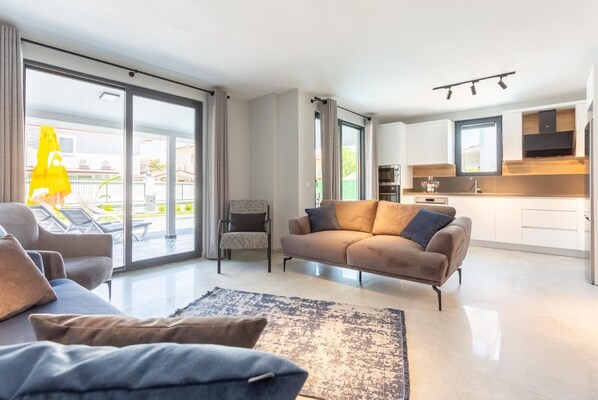A modern living room with a sofa, armchairs, and a coffee table. There is a sliding glass door leading to a balcony with a yellow umbrella. - Villa Exclusive Paradise 3 (Dalyan)