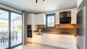 Une cuisine moderne avec des meubles blancs, des appareils en acier inoxydable et une grande fenêtre donnant sur un espace patio.