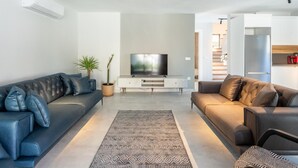 Een moderne woonkamer met twee banken, een televisie en een trap die naar een keuken leidt.