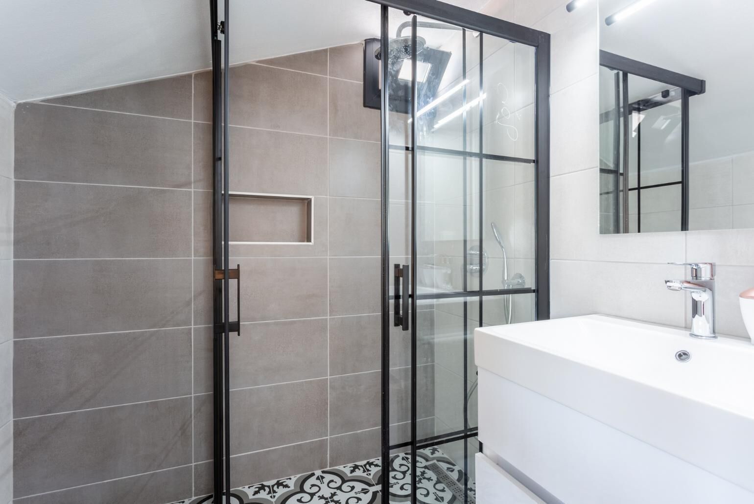 A modern bathroom with a glass-enclosed shower, a white sink, and a mirror above the sink.