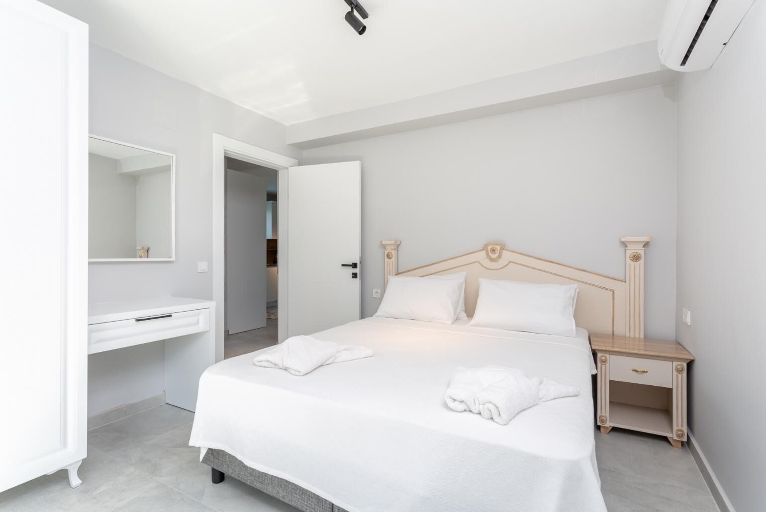Um quarto com cama, mesa de cabeceira, cómoda e espelho.