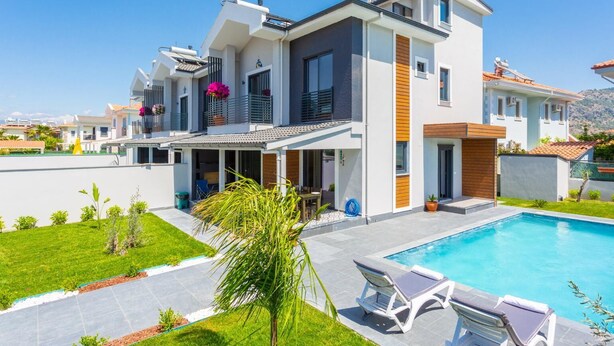 Een modern huis met twee verdiepingen, een zwembad, buitenzitplaatsen en een verzorgde tuin.
