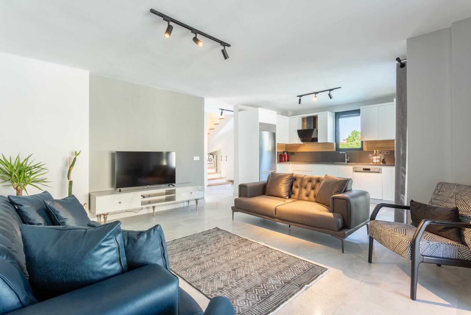 Een moderne woonkamer met een flatscreen televisie, een bank en een kamerbreed tapijt met dessin.
