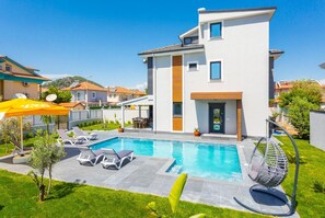 A modern two-story house with a swimming pool, outdoor seating, and a garden.