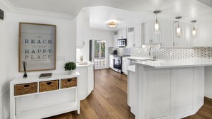 Une cuisine moderne avec des meubles blancs, un plan de travail en marbre et un îlot central intégré. Un tableau encadré est accroché au mur et une petite plante est posée sur le plan de travail.