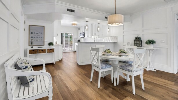 Une cuisine spacieuse dotée de meubles blancs, d’un îlot central et d’un coin repas avec des chaises blanches et une table ronde.