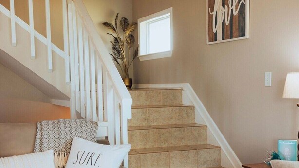 A living room with a beige sofa, a staircase, and a wall with a 'love' sign.