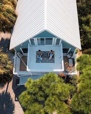 A two-story house with a balcony, surrounded by pine trees.