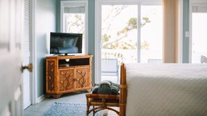 A bedroom with a bed, a television on a wooden cabinet, and a view through a sliding glass door.