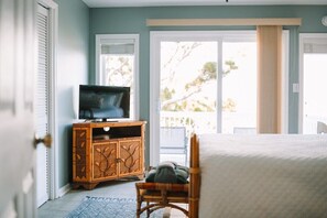 A bedroom with a bed, a television on a wooden cabinet, and a view through a sliding glass door.