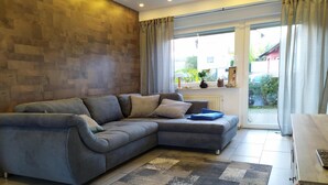 A modern living room with a grey sectional sofa, a wooden coffee table, and a view through a glass door to the outdoors. - Fantastic view high above the Rhine (Bacharach)