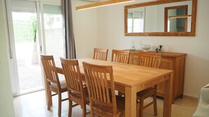 Un comedor con mesa y sillas de madera, un espejo grande y una zona de cocina con armarios y encimera.