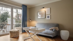 Un salon avec un canapé gris, une table basse blanche, un pouf à motifs léopard, un vase blanc et un tableau encadré accroché au mur.