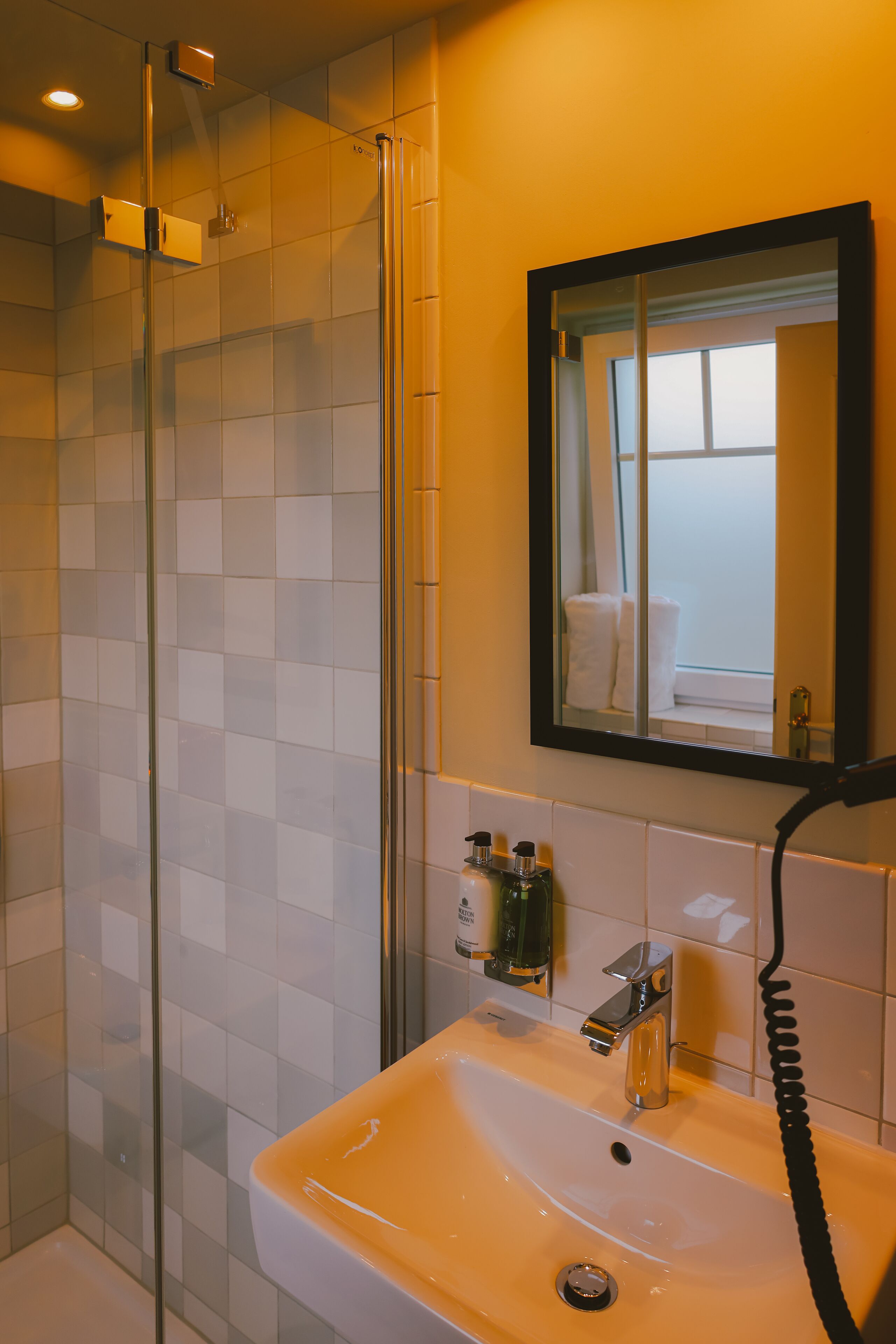A bathroom with a glass shower enclosure, a sink with a mirror above it, and toiletries on the wall.