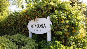 Un letrero que dice 'Mimosa House' rodeado de exuberante follaje.