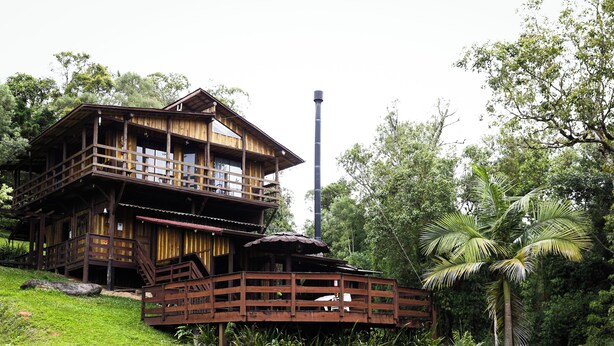 A wooden multi-story house with balconies, a chimney, and a thatched-roof structure. - Holo Pousada Vale Encantado (Rancho Queimado)