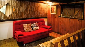 Un sofá rojo con cojines estampados, un banco de madera, una pared de madera con tablones verticales y un cuadro enmarcado de un caballo.