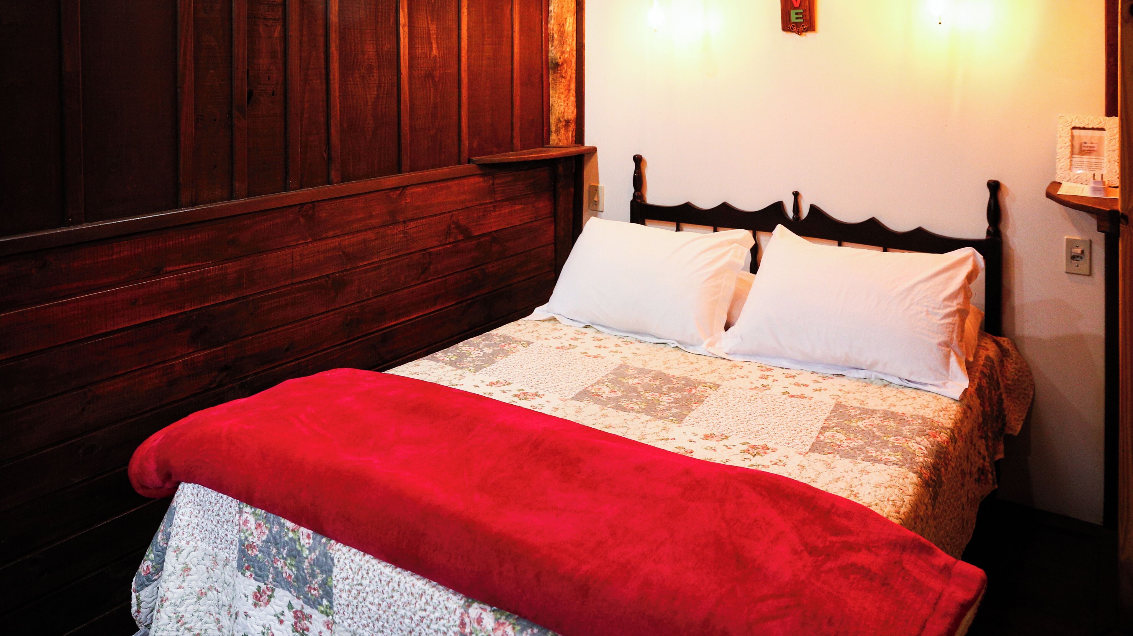 A wooden bed with a floral quilt, a red blanket, and a wooden headboard.