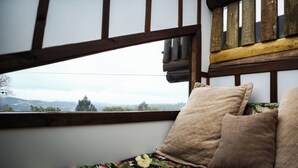 A room with a view through a window, wooden beams, and a bed with patterned bedding. - Holo Pousada Vale Encantado (Rancho Queimado)