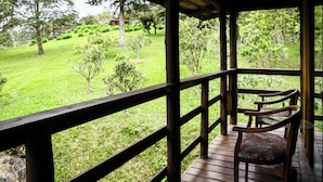 A wooden deck with a glass table and chairs, overlooking a lush green garden with various trees and shrubs. - Holo Pousada Vale Encantado (Rancho Queimado)