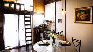 A dining area with a round table set for two, a vase with flowers, and a kitchen in the background. - Holo Pousada Vale Encantado (Rancho Queimado)