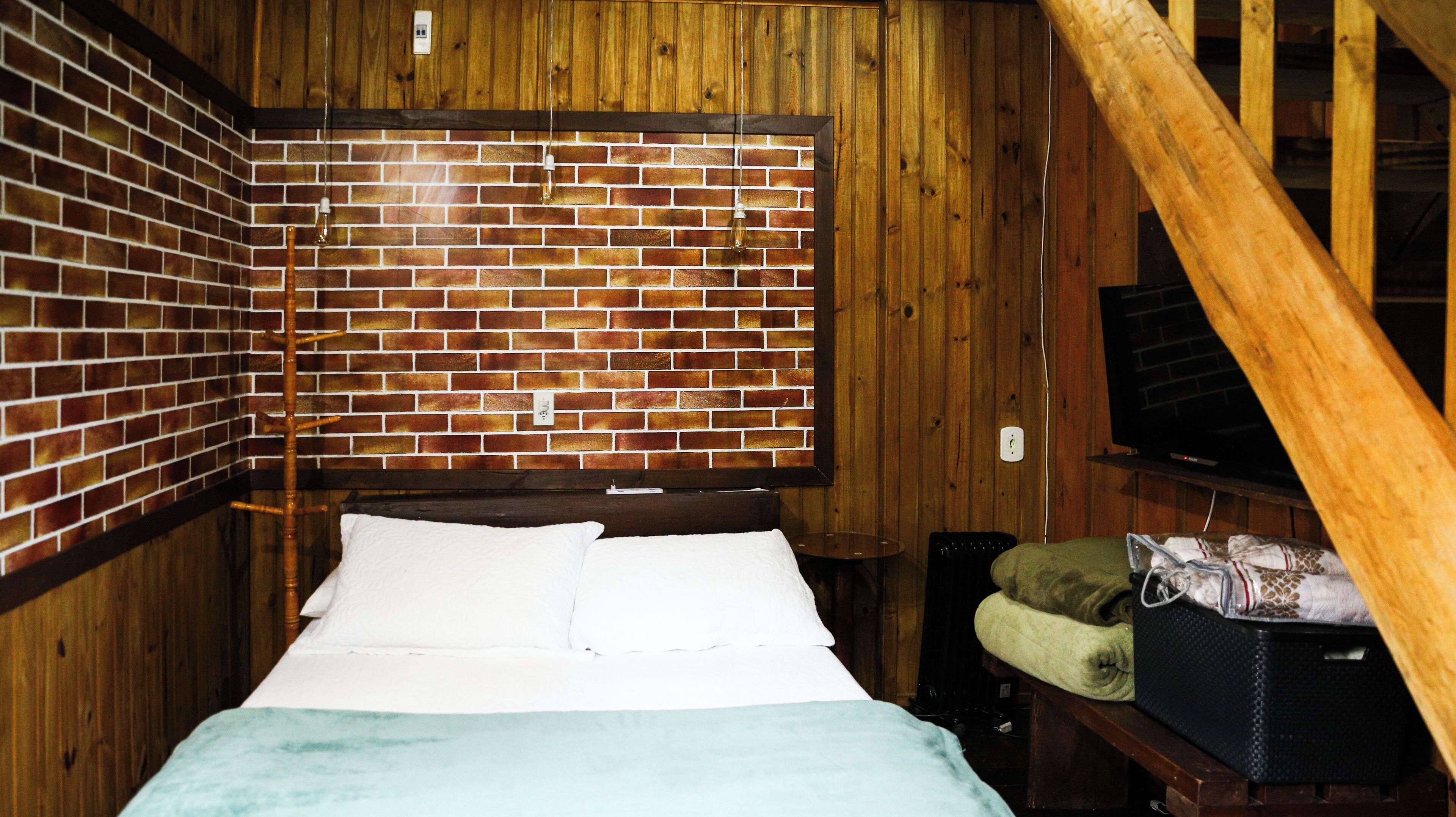 A room with a brick wall, a bed with white linens, a wooden ceiling, and a television on a stand.