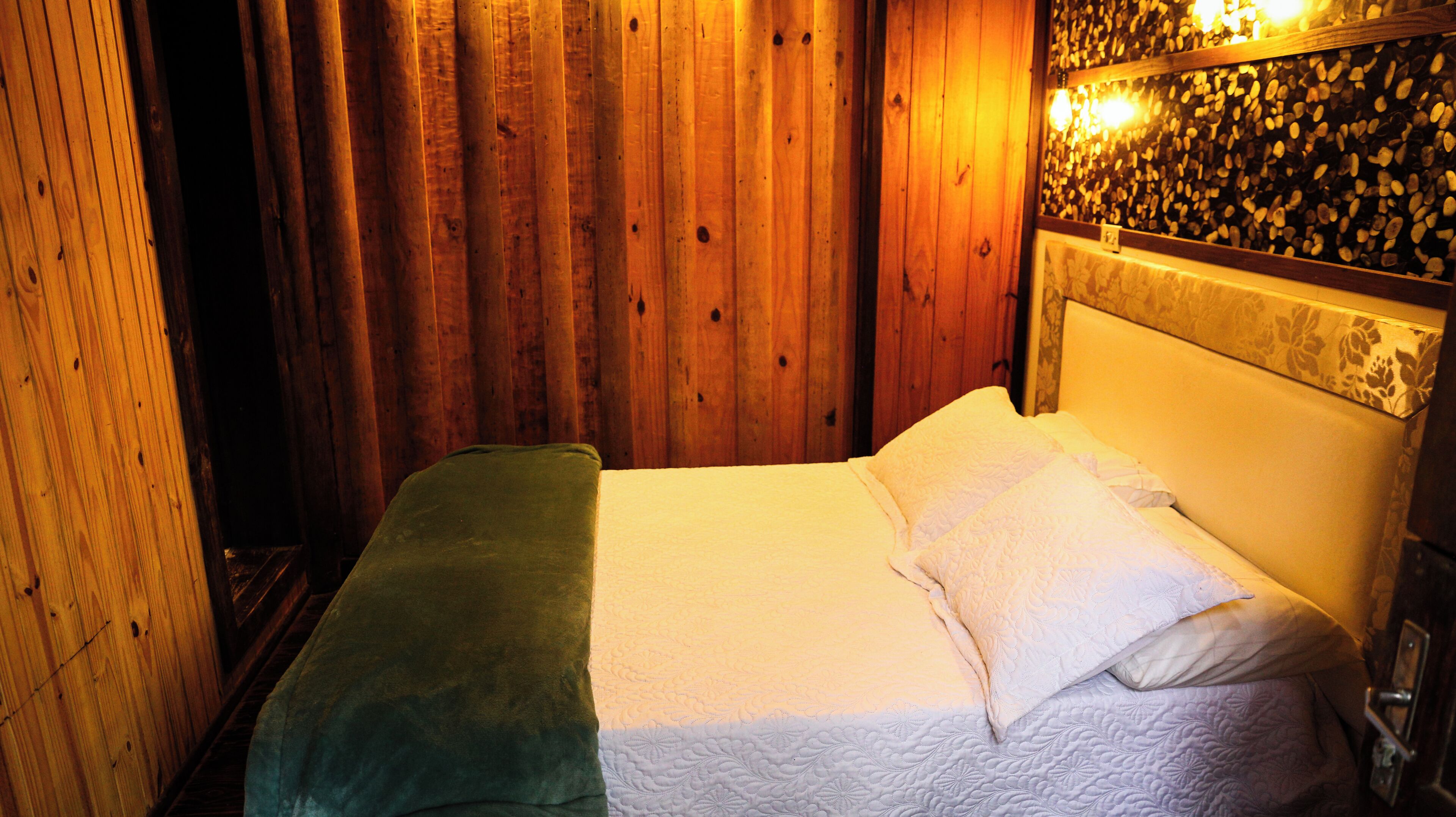 A wooden room with a bed, a green blanket, and a wall with a textured pattern.