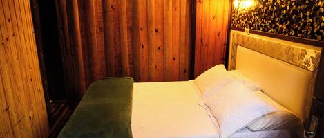 A wooden room with a bed, a green blanket, and a wall with a textured pattern.