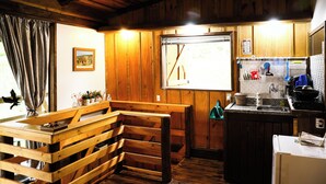 A rustic kitchen with wooden walls, a bench, a window with a view, and basic kitchen amenities. - Holo Pousada Vale Encantado (Rancho Queimado)