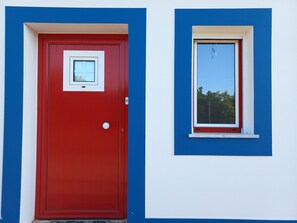 A red door with a small window above it, set against a blue and white wall.