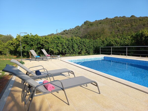 A swimming pool with lounge chairs and a view of a forested hillside.