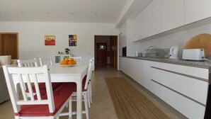 Une cuisine moderne avec des meubles blancs, une table à manger avec des chaises rouges et un panier de fruits.