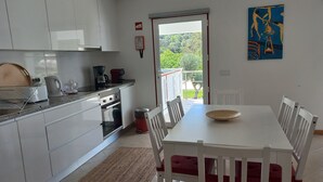 Une cuisine moderne avec des meubles blancs, une table à manger entourée de chaises rouges et une vue sur la verdure à l’extérieur.