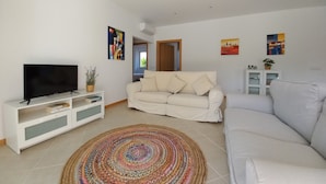 Un salon avec un téléviseur à écran plat posé sur un meuble TV blanc, un canapé beige, un tapis coloré et un meuble blanc orné d’une plante.