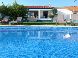 A swimming pool with clear blue tiles, a covered outdoor seating area with lounge chairs, and a building with a red-tiled roof in the background. - 3-Bedroom Villa in Silves (Silves)
