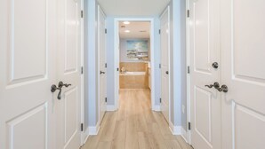A hallway with white doors and light blue walls leading to a bathroom with a bathtub and a painting on the wall. - 2B Gulf Front*Tower 5*Stunning Views (Pensacola Beach)