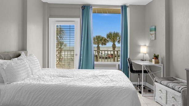 Une chambre d’hôtel avec un lit, un bureau, une chaise et une vue sur la plage et les palmiers.