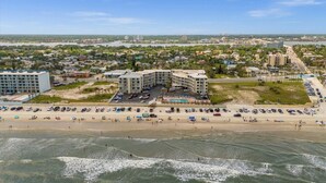 Vue aérienne d’un hôtel situé sur la côte, composé de plusieurs bâtiments, avec une plage et un parking.