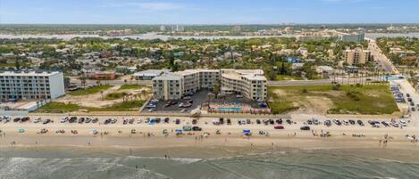 Vue aérienne d’un hôtel situé sur la côte, composé de plusieurs bâtiments, avec une plage et un parking.