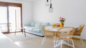Un salon lumineux avec un canapé bleu clair, une table ronde entourée de chaises en osier et une petite table d’appoint.