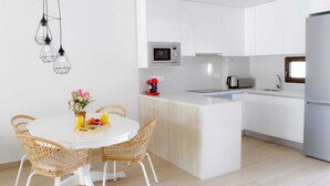 Une cuisine moderne avec des meubles blancs, un îlot central, un four à micro-ondes et un réfrigérateur en acier inoxydable.