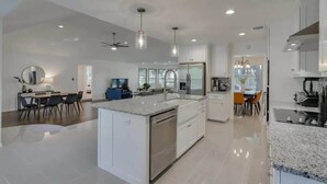 Una cocina moderna con una isla central, armarios blancos y electrodomésticos de acero inoxidable.