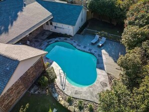 A residential backyard with a swimming pool, stone patio, and a wooden deck.