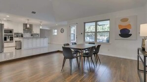Una cocina moderna con armarios blancos, una isla central y un comedor con mesa y sillas de madera.