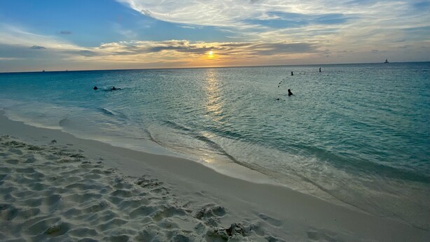 A beach with clear water, a sunset, and a distant ship.