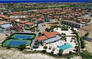 A resort with multiple buildings, a tennis court, a swimming pool, and a beach area.