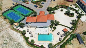 An aerial view of a resort with a swimming pool, tennis courts, and a large building with a red roof.